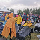 Paljon ihmisiä pukeutuneina sadevarusteisiin festivaalialueella ulkona.