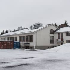 Vanhan koulurakennuksen edessä on lumipenkkoja ja merikontteja.