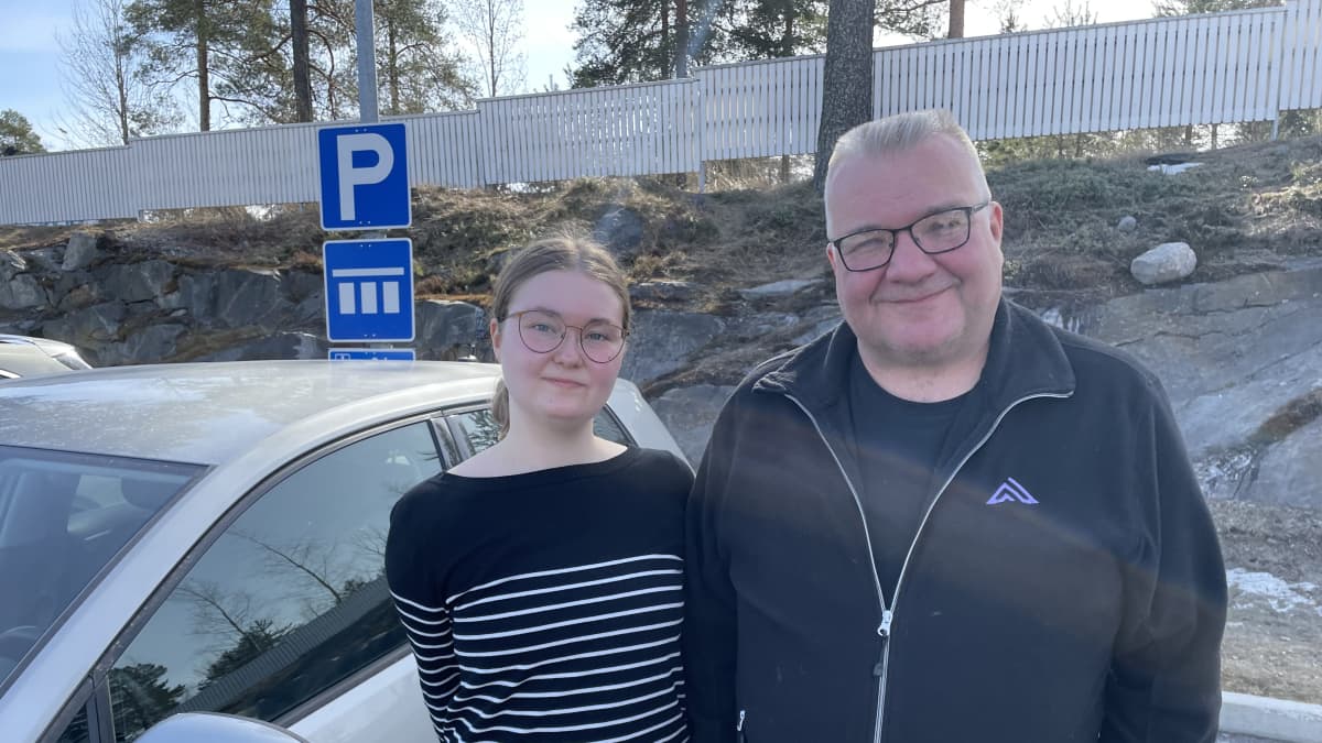 Autokoulua käyvä Jenna Kovalainen ja opettaja Mika Juntunen seisovat auton vieressä. 