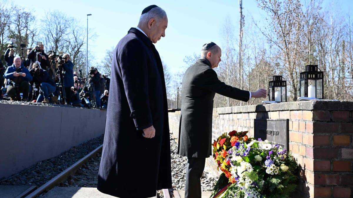 Kaksi tummaan pukeutunutta miestä asettaa seppeleitä muistomerkille.