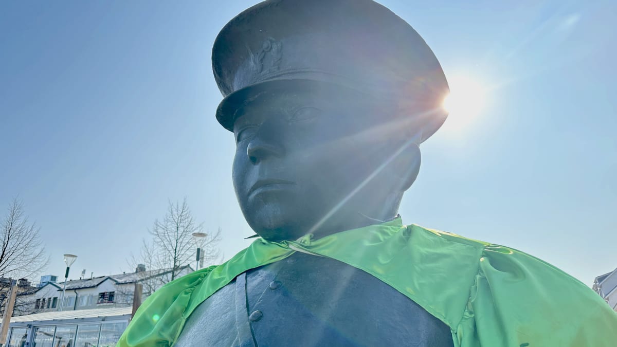 Oulun toripolliispatsas Oulun torilla aurinkoisena päivänä, päällään vihreä "muskelibolero" jossa piikkejä kauluksessa. 
