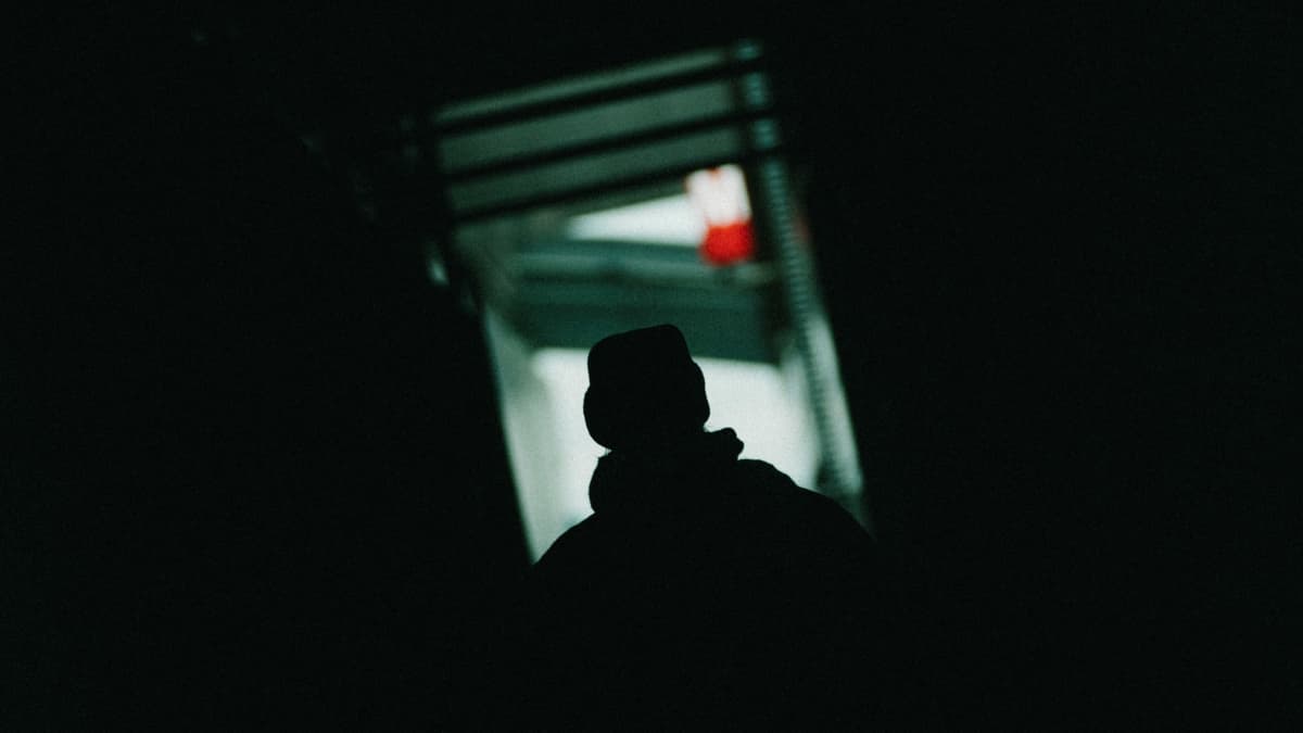 Anonyymi henkilö seisoo pimeässä käytävässä.