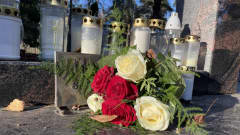 Punavalkoinen ruusukimppu ja muistokynttilöitä hautausmaan muistopaikalla.