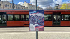 Jääkiekon MM-kisojen karttaopaste kiinnitettynä tolppaan Tampereen keskustassa. Taustalla kulkee punainen ratikka.