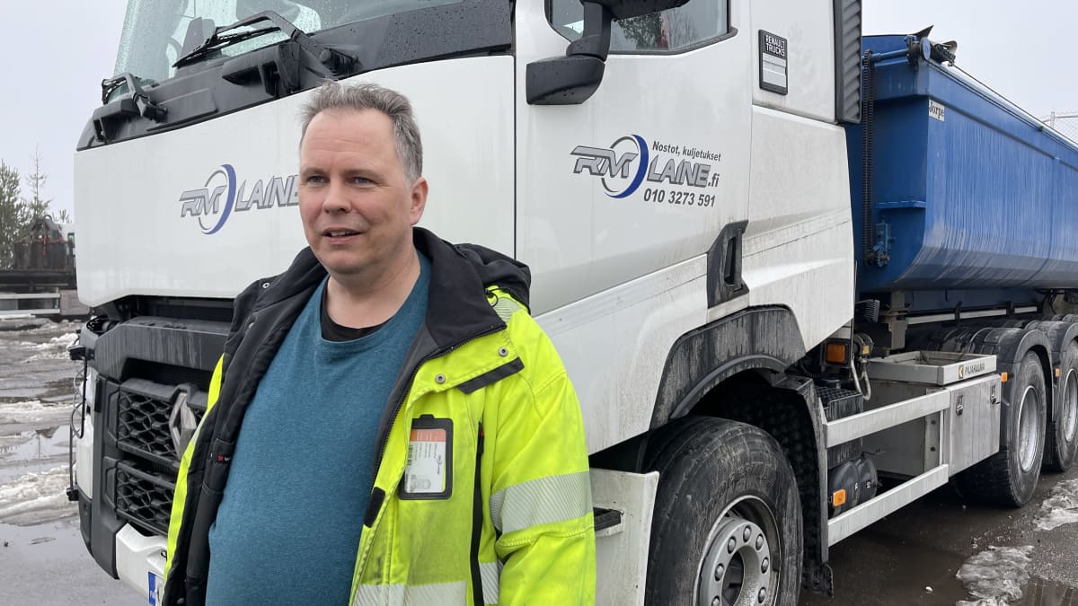 Nosto- ja kuljetuspalveluyrittäjä Mikko Laine seisoo kuorma-auton edessä lumisateessa ja hymyilee.