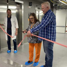 Kaksi miestä ja yksi nainen leikkaavat punaista nauhaa uudessa sairaalarakennuksessa. 