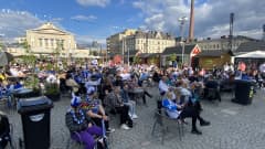 Tampereen Keskustorin Kesäkeidas-alue täynnä Suomi-faneja seuraamassa peliä screeniltä. Torialue täynnä pöytiä ja tuoleja, sekä myyntikojuja. Aurinko paistaa.
