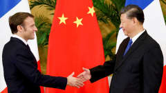 Puolikuvassa kaksi pukuun pukeutunutta ihmistä kättelee. Taustalla Kiinan ja Ranskan liput. 