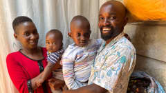 Kenialainen perhe poseeraa kotinsa ovensuussa. Äiti, isä ja kaksi pientä lasta. 