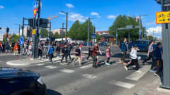 Lapsia ja nuoria ylittämässä suojatietä Tampereen keskustassa. Aurinko paistaa kirkkaalta taivaalta.