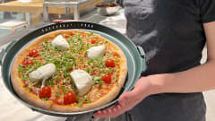 Henkilö pitelee muoviseen rasiaan pakattua pitsaa, jossa on päällä muun muassa pikkutomaatteja ja mozzarella-juustoa.