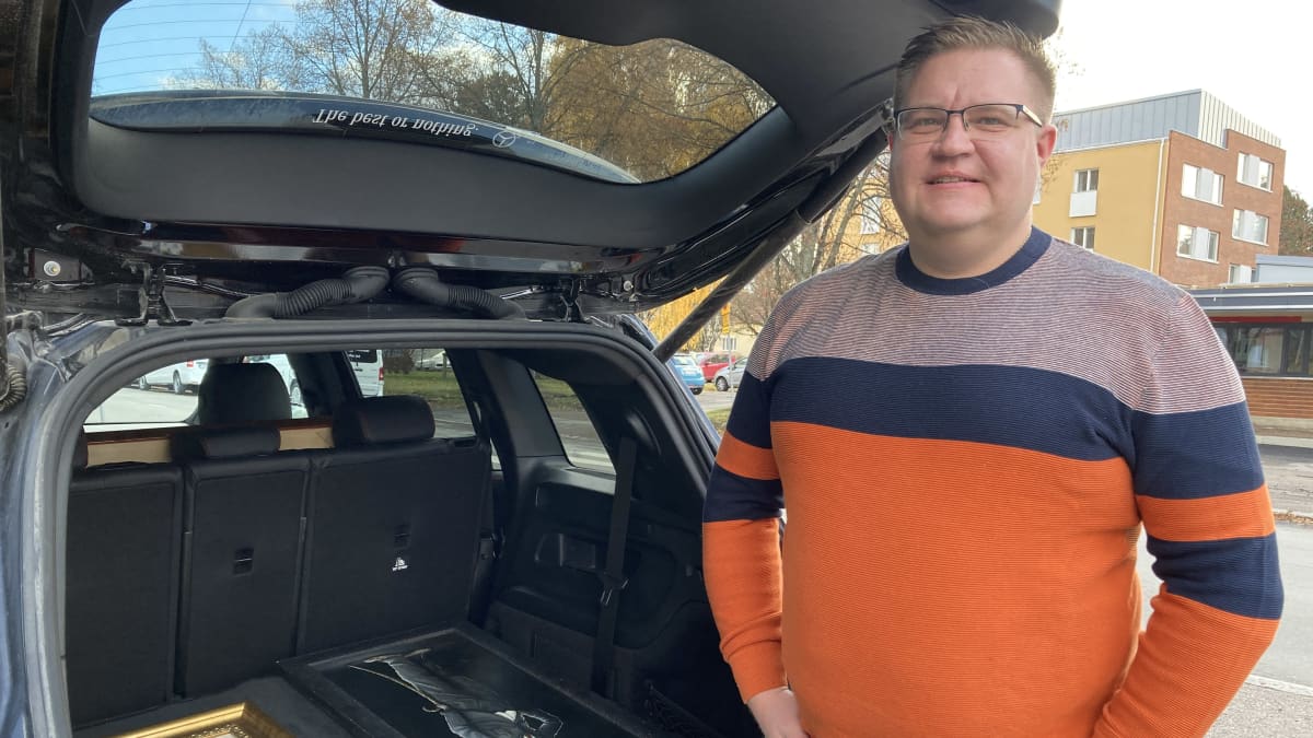 Toni Saarimäki seisoo autonsa vieressä, auton takaluukku on auki ja siellä on tauluja.