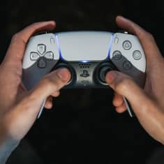Playstation 5 pelikonsolin ohjain pelaajan käsissä.