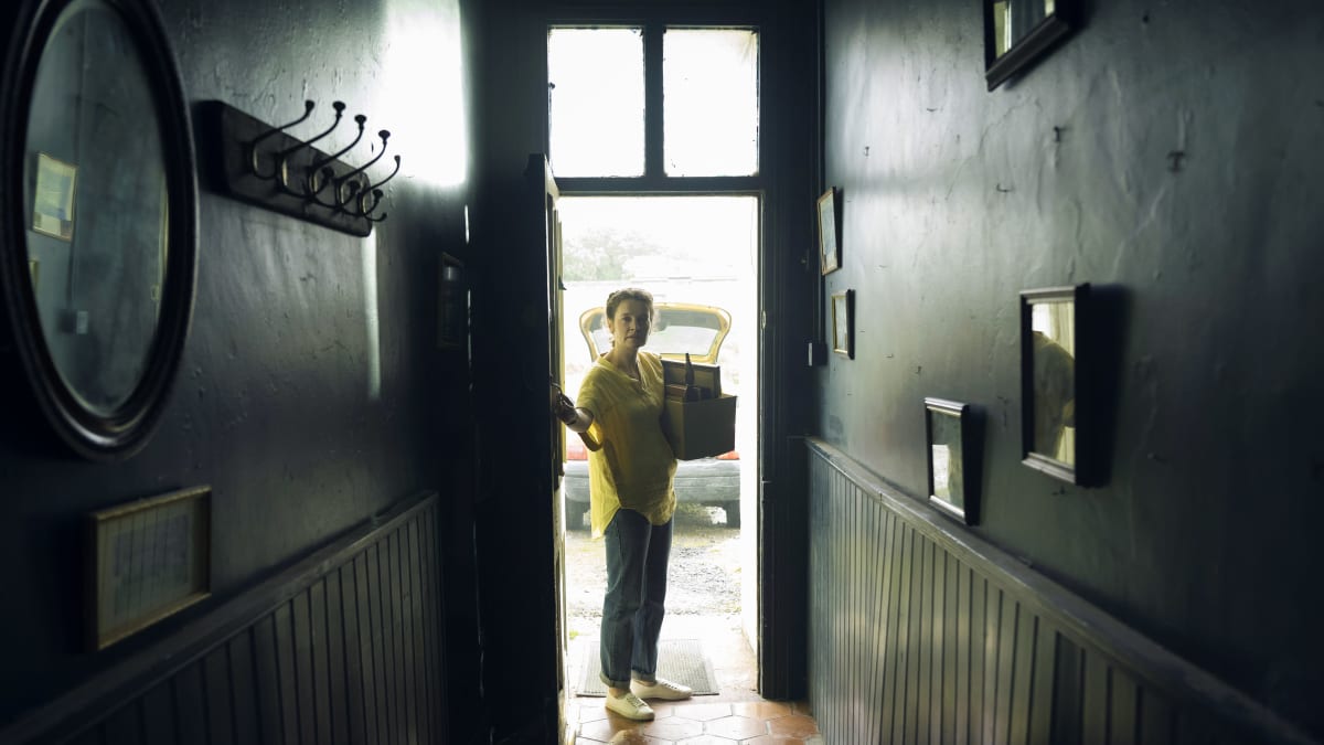 Grace (Catherine Walker) står vid en ytterdörr och ser in mot en mörk korridor.
