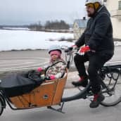 Isä Panu Rintamäki polkee laatikkopyörällä. Lyyti-tytär istuu kyydissä.
