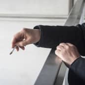 På bilden syns en hand som håller i en cigarrett. Handen ser ut att tillhöra en man som står på en balkong.