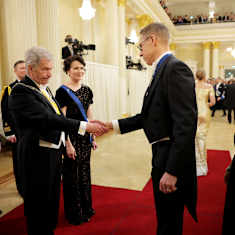 Alexander Stubb shaking hands with Sauli Niinistö on a red carpet, alongside their spouses. All are dressed in formal wear or gowns.