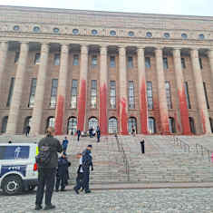 Finland's Parliament House pillars splattered red, with police officers, a police vehicle and other people in the foreground.