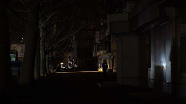 Henkilö kulkee pimeällä kadulla Odessassa, vain muutama valokaistale näkyy.