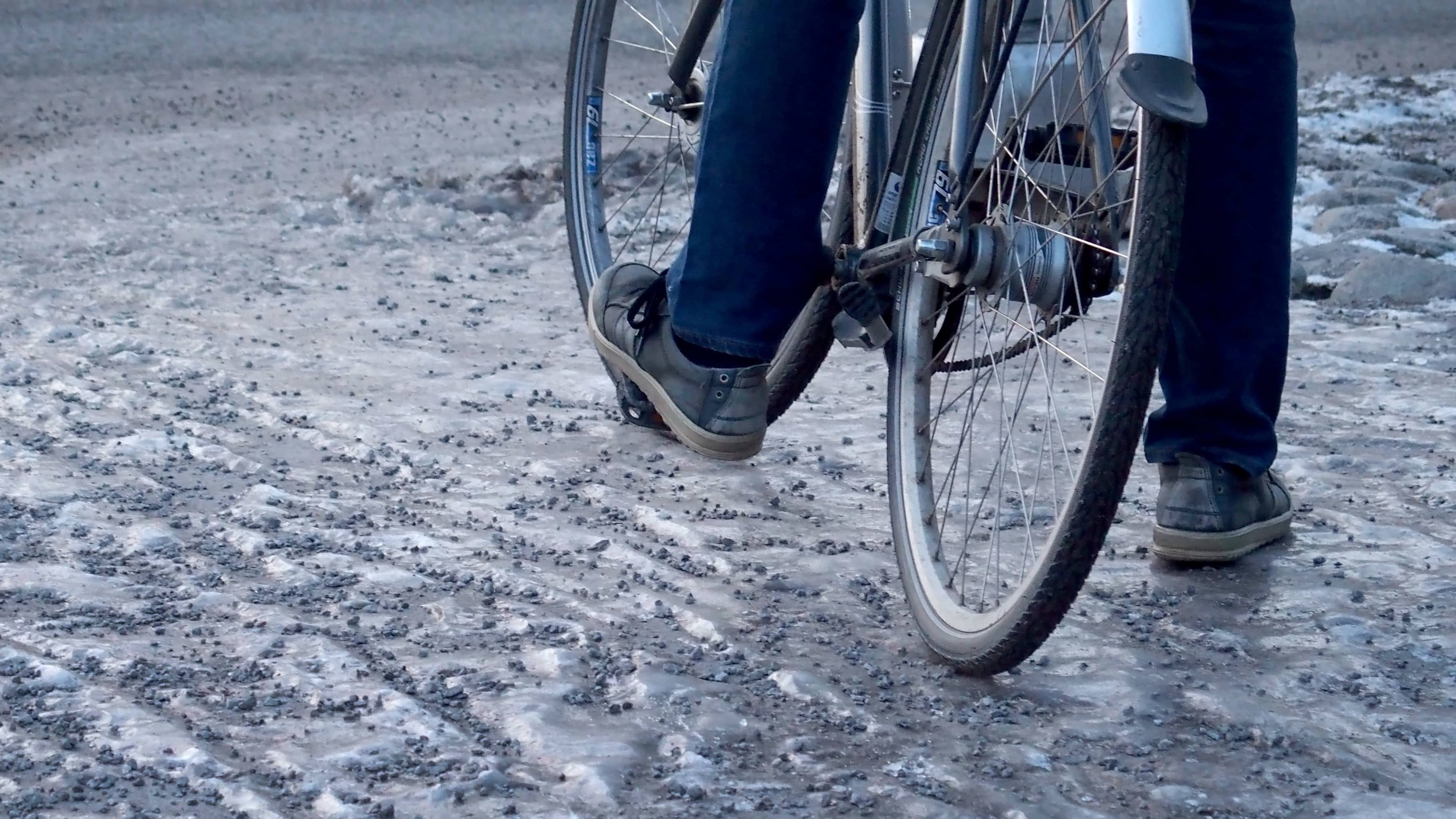 En cyklist har stannat till på en isig cykelväg på vilken man spridit ut grus för att bekämpa halkan. 