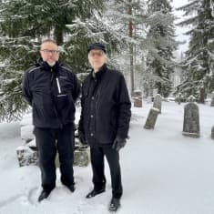 Kaksi miestä seisoo hautausmaalla.
