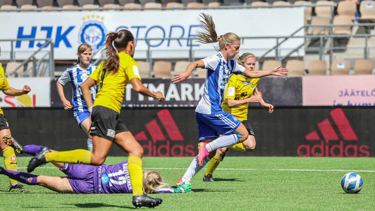Linda Sällström i blåvitrandig tröja driver med bollen mot KuPS. Hon jagas av KuPS-spelare i gula tröjor. En HJK-spelare har fallit till marken.