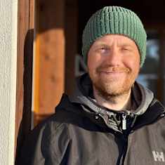Mies hymyilee kameralle. Aurinko paistaa hieman silmiin. 