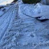 Asuinalueella tie on pehmenneen lumen ja sohjon peitossa. Lumeen on jäänyt paljon jälkiä renkaista. Kuvassa oikealla myös lumikola, jossa lunta. 