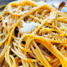 Lautasellinen keitettyä spagettia, jonka päällä on parmesaania.