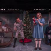 Kolme miestä ja yksi nainen joulukuusen vieressä lahjoja purkamassa.