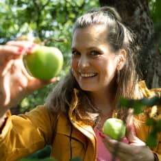 Nainen näyttää kameralle kahta omenaa. 