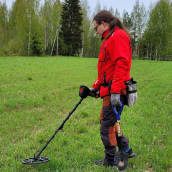 Mies käyttää metallinpaljastinta tutkiessaan peltoa.