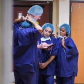 Sjukskötare och kirurger i kirurgutrustning står och pratar med varandra i en sjukhuskorridor.