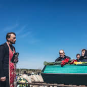 Pappi ja hautajaisvieraita arkun äärellä hautausmaalla.