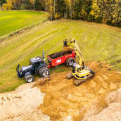 Traktori ja kauhakuormaaja levittämässä pellolle ruskealta hiekalta näyttävää maanparannuskuitua.
