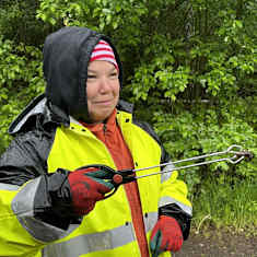 Henkilö kerää etanoita tien varresta käyttäen roskapihtejä. Hänellä on yllään kirkkaan keltainen sadetakki.