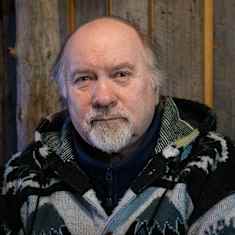 Lähikuva Pekka Aikiosta. Takana hirsinen seinä.