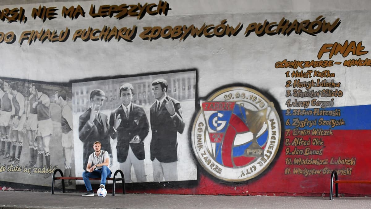 Richard Jensen sitter på en bänk framför en muralmålning, som är en hyllning till cupvinnarcupens final mellan Gornik Zabrze och Manchester City år 1970.