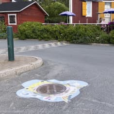 Koristeltu kaivonkansi ja taustalla ihmisiä istumassa terassilla Kemin sisäsatamassa.