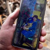 Miehen kädessä puhelin jossa kuva naisesta koira sylissä