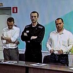 Kuva ruudulta, jossa Alexei Navalnyi seisoo pöydän ääressä vieressään kolme muuta ihmistä.