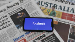 En mobiltelefon med texten facebook på skärmen. Mobiltelefonen ligger på en hög med tidningar från Australien.