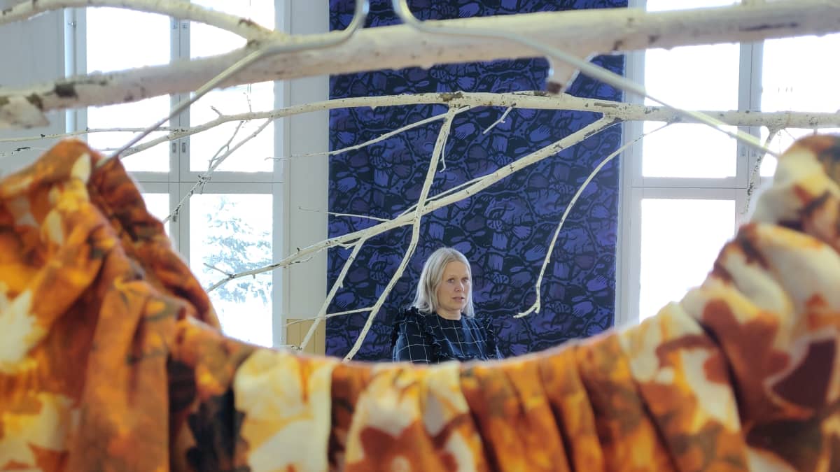 Paola Suhonen suuressa näyttelytilassa keskellä erilaisia kankaita.