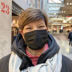Nainen seisoo kauppakeskuksessa kasvomaski kasvoillaan.
