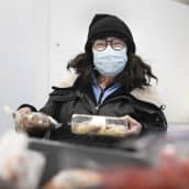 Jyväskyläläinen Sirkku Duruji katsoo kameraan. Hänellä on käsissään ruoka-avussa tarjolla olevaa leivonnaispakkauksia.