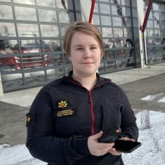 Palomestari Oona Englund seisoo Kokkolan paloaseman edustalla kädessään kännykkä ja virve