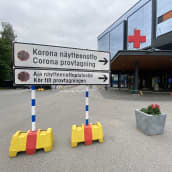 En skylt till corona provtagning. I bakgrunden ses en sjukhusbyggnad.