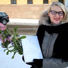 Heta-Leena Sierilä poseeraa kameralle viittomakieliteko-palkinnon ja kukkien kera talvisessa ympäristössä.