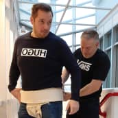 Sumopainija Oskari Riihioja ja sensei Sami Ylä-Kero näyttävät, miten noin 5-metrinen mawashi puetaan