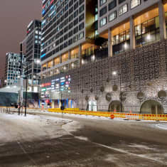 Fasaden på ett köpcentrum, fotat från andra sidan av en väg. Vid fasaden finns röd-gula staket som stoppar fotgängare från att gå på trottoaren. I bakgrunden syns en lyftkran. Det är mörkt ute, och lite snö på marken.
